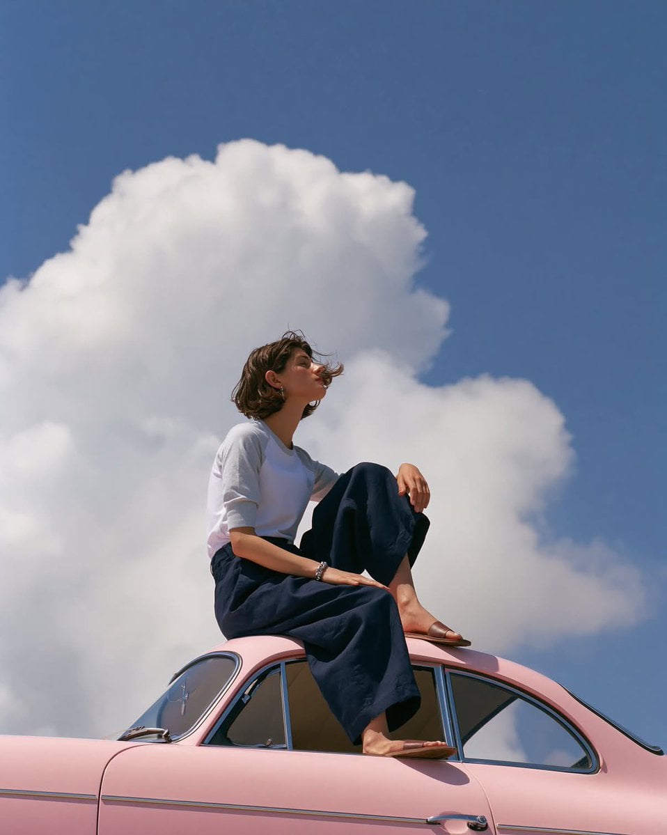 A dreamy editorial fashion photograph of a minimalist young woman sitting gracef